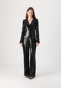 Black sequined jumpsuit with a V-neck, long sleeves, tailored fit, and straight legs, reflecting light with a glossy texture.