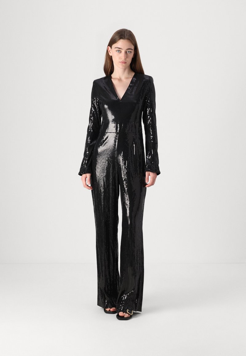 Black sequined jumpsuit with a V-neck, long sleeves, tailored fit, and straight legs, reflecting light with a glossy texture.