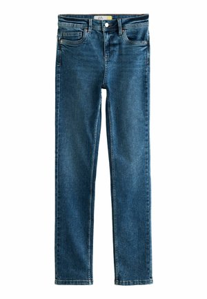 Primer plano de una persona que lleva jeans azul oscuro y una camisa a rayas, con anillos en la mano derecha descansando sobre su muslo.