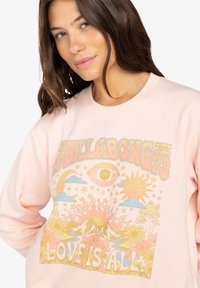 Hellrosa Sweatshirt mit Rundhalsausschnitt, das einen zentralen Grafdruck von Sonne, Bergen, Blumen und dem Text "DIE LIEBE IST ALLES" in fetten Buchstaben zeigt.