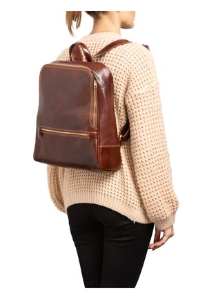 Zaino in pelle marrone con finitura liscia, forma rettangolare, tasca frontale con zip e spallacci regolabili, indossato da una persona.