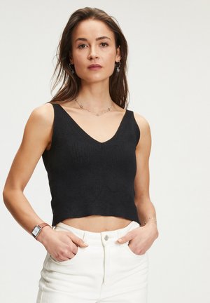 Top court noir à côtes avec un décolleté en V, associé à un pantalon blanc taille haute. Le tissu semble texturé et ajusté.