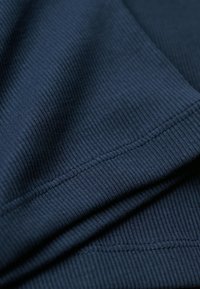 Tissu côtelé bleu marine avec une texture douce et des coutures visibles. Le matériau se plie pour montrer de la profondeur et un motif cohérent avec le côtelé.