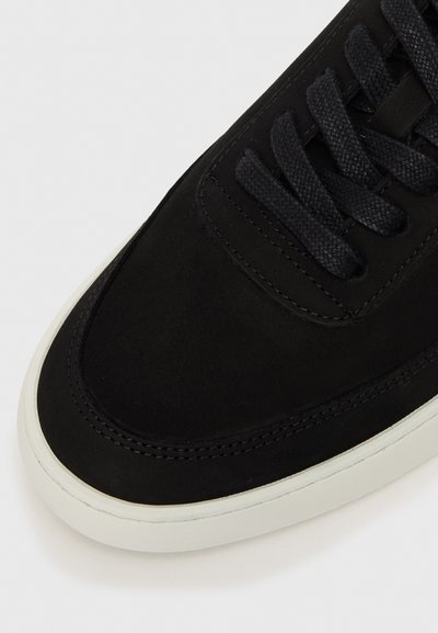 Crne antilop tenisice s okruglim vrhom, teksturiranim crnim vezicama i bijelim gumeni potplat. Šavovi oko ruba dodaju detalje.