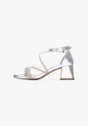 Sandalia de tacón de bloque metálico plateado con tiras finas acentuadas con piedras de brillo y cierre de hebilla en el tobillo.
