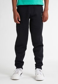 Sorte joggerbukser med en tætsiddende pasform, der har to sidelommer, elastiske manchetter og en struktureret talje. Sammen med hvide sneakers.
