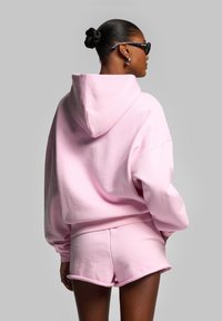 Felpa con cappuccio rosa dal fit oversize e polsini a coste, abbinata a pantaloni corti coordinati, entrambi realizzati in morbido tessuto di cotone.