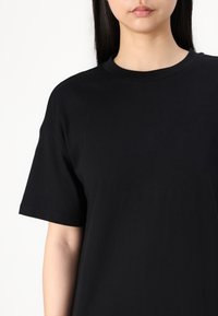 T-shirt en coton noir avec un col rond et des manches courtes. Texture lisse sans motifs ni accents visibles.