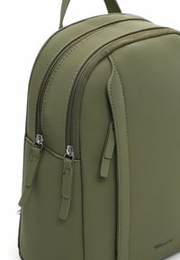 Plecak oliwkowo-zielony z gładkiej tkaniny, z dwoma suwakami i subtelnym przeszyciem. Posiada dwa boczne suwaki oraz górny uchwyt do przenoszenia.