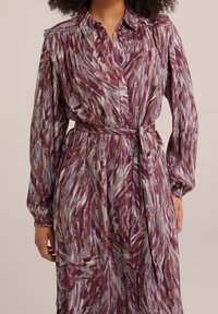 Long-sleeve dress in a swirling pattern of purple, blue, and gold. Features a collared neckline, button front, and matching belt for waist definition.