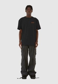 Sort bomulds t-shirt med et orange logo, parret med grå cargo bukser med flere lommer og justerbare manchetter, fuldendt med sorte sneakers.