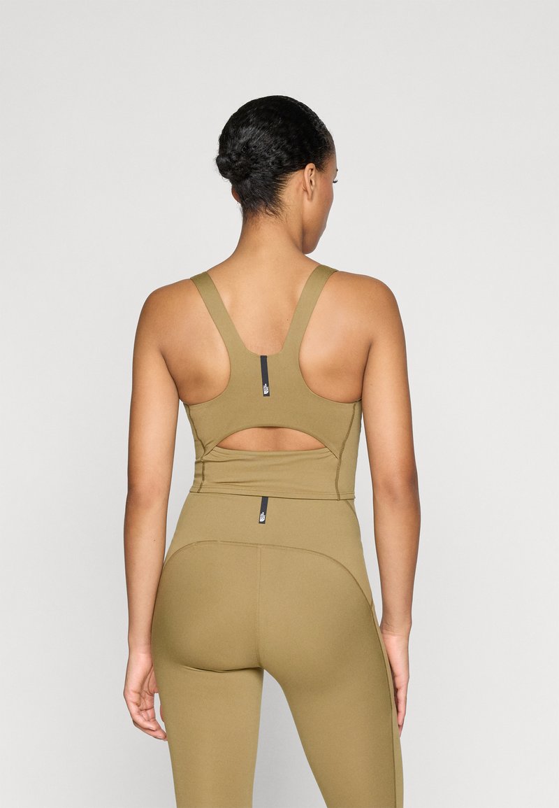 Olive green athletic tank top with a racerback design, featuring a cutout on the back and subtle hardware accents. Paired with matching leggings.
