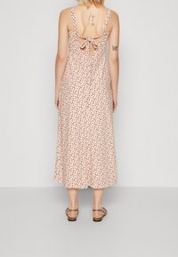 Vestido midi floral en crema con flores rojas. La parte de atrás presenta un cierre con lazo y un detalle de corte. Tirantes finos y corte relajado.
