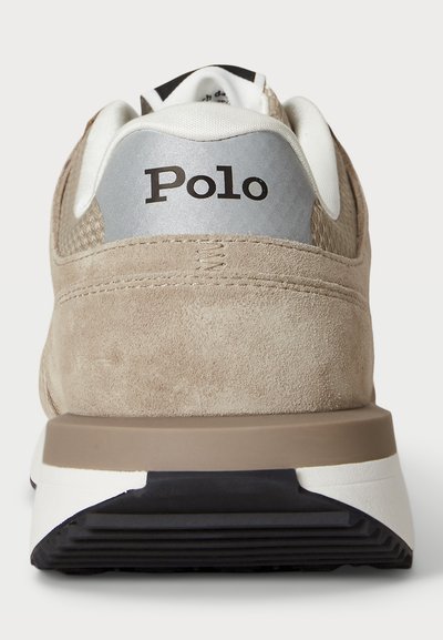 Svetlo smeđi suede tenesici s bijelim i crnim potplatom, mrežastim detaljima i srebrnom petom koja sadrži "Polo" logo. Teksturirani gornji dio za prozračnost.