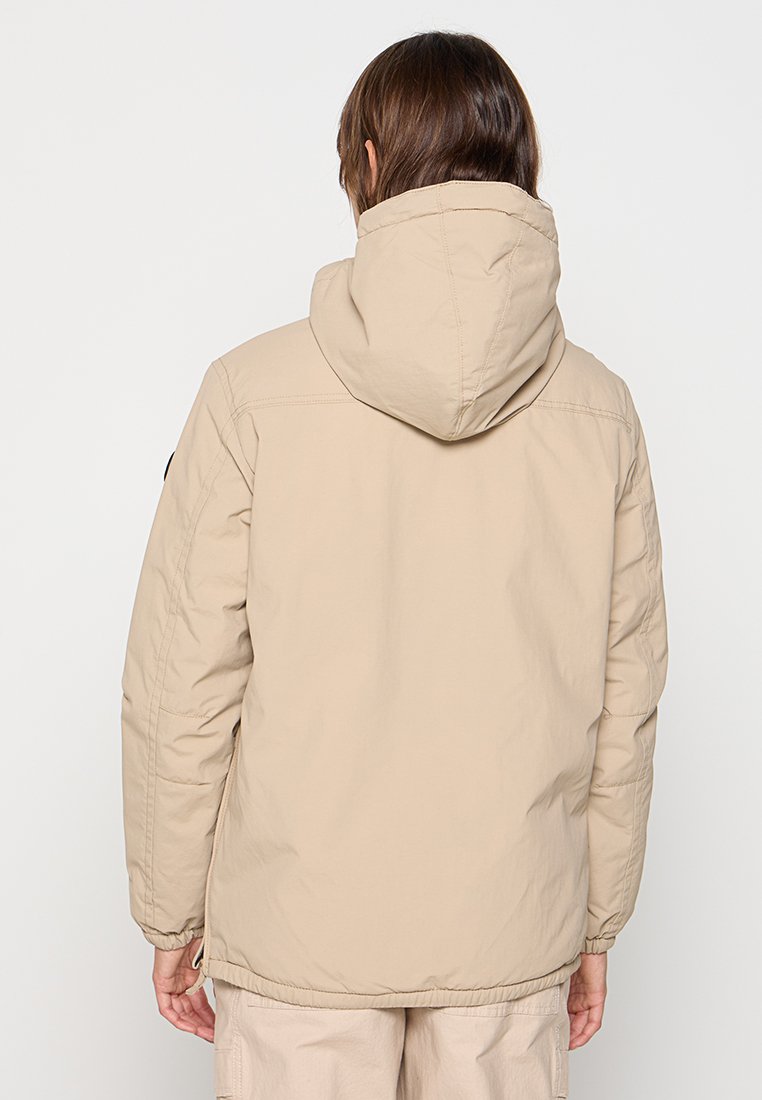 Beige hoodie met een zachte textuur, elastische manchetten en een trekkoord aan de zoom; heeft een minimalistisch ontwerp zonder zichtbare logo's.