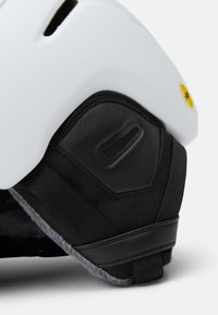 Weißer Helm mit einem schwarzen gepolsterten unteren Abschnitt, der über Belüftungsöffnungen und eine strukturierte Oberfläche verfügt. Auffälliges gelbes Mips-Logo an der Seite.