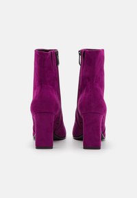 Ett par lila mockakängor med klack och bakre dragkedjor på en vit bakgrund.