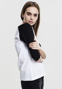 Svart og hvit raglan t-skjorte med trekvartslanger, myk bomullsstoff, avslappet passform, svak bue ved kanten og enkel design.