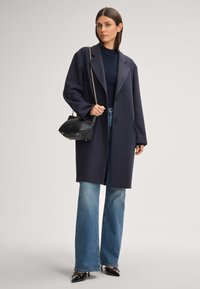 Marineblauwe wolmixjas met een ingesneden kraag en twee knopen, gecombineerd met lichtblauwe flare jeans en een zwarte handtas. Glanzende puntige schoenen.