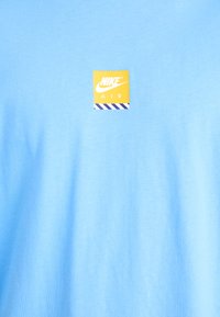 Light blue cotton t-shirt featuring a square yellow Nike Air logo with a striped border. Soft texture and crew neck design.