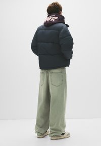 Jachetă pufoasă de culoare bleumarin închis, cu un design matlasat, purtată peste un hanorac vișiniu. O pereche de blugi verzi deschis, largi și adidași crem.