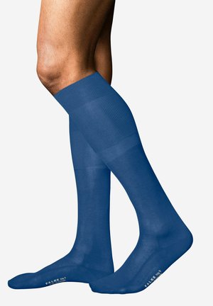 Benendie kniehoog, halftransparante blauwe compressiekousen dragen met "FALKE No9" gedrukt nabij de tenen, tegen een effen witte achtergrond.
