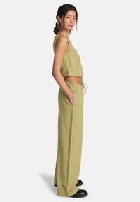 Ensemble deux pièces vert olive avec des rayures verticales. Le haut court est doté d'une fermeture à boutons, tandis que le pantalon possède une taille élastique et des poches.