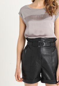 Top de satén gris de mangas cortas combinado con pantalones cortos de cuero negro de cintura alta que cuentan con un cinturón y puños enrollados.