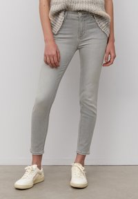 Jeans ajustados de color gris claro con una textura suave y desgastada, con un talle medio y tobillos recortados, combinados con zapatillas blancas.