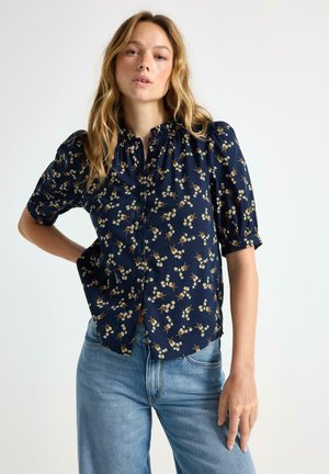 Blusa floreale blu navy con maniche a sbuffo corte, caratterizzata da un collo rotondo e chiusura a bottoni. Tessuto leggero con un motivo testurizzato.