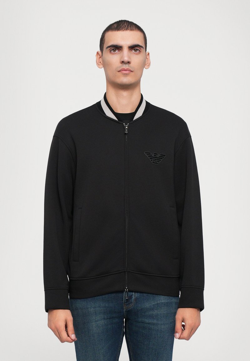 Must linnane zip-up bomber-jakk, millel on soonikkoelus ja tagasihoidlik logopatch. Valmistatud pehmest kangast, küljetaskutega ja lõtkus lõikega.
