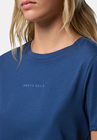 T-shirt di cotone blu con scollo rotondo e maniche corte, con la scritta "NORTH SAILS" di un blu più chiaro, posizionata sul petto.