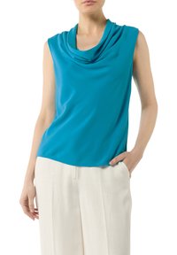 Top bez rękawów w intensywnym turkusowym kolorze z opadającym dekoltem, połączony z jasnymi, szerokimi spodniami. Gładka faktura.