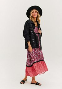 Czarna dżinsowa kurtka na wzorzystą różową sukienkę maxi z koronkowym wykończeniem, w połączeniu z czarnymi klapkami i szerokim, czarnym kapeluszem.