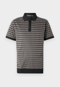 Lühikese varrukaga polo särk, millel on musta ja beeži värvi houndstooth muster, ühtlane must krae ja mansetid ning kolme nupuga sulguri.