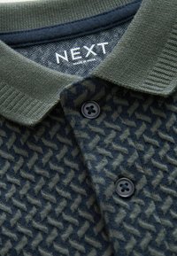 Polo in verde scuro e navy con un tessuto a trama e motivo. Presenta un colletto a costine e due chiusure con bottoni neri. Etichetta del marchio visibile.