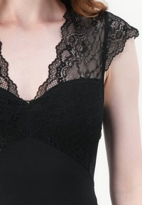 Black dress featuring a deep V-neck and lace cap sleeves. The bodice combines sheer lace with solid fabric, showcasing intricate floral patterns.