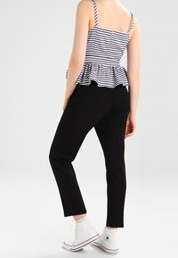 Pruhovaná peplum top s nastavitelnými ramínky, přiléhavým trupem a volánkovým pasem. Černé zúžené kalhoty. Bílé vysoké tenisky s červenými akcenty.