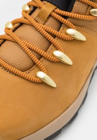 Stivale da trekking color tortora con upper in pelle texturizzata e mesh, con lacci a motivo arancione e marrone e dettagli in oro.