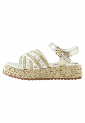 Sandały na koturnie z krzyżującymi się paskami, metalicznymi złotymi akcentami i plecioną podeszwą z juty. Posiadają regulowany pasek wokół kostki oraz biały materiał z logo.
