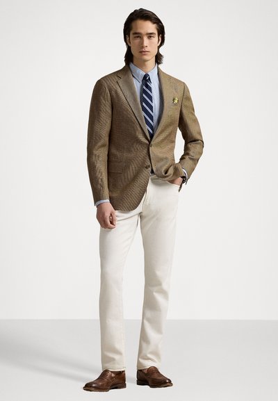 Bruine visgraat blazer, blauw gestreept overhemd, marineblauwe das, crèmekleurige broek, bruin leren schoenen, pochet met gele accenten.