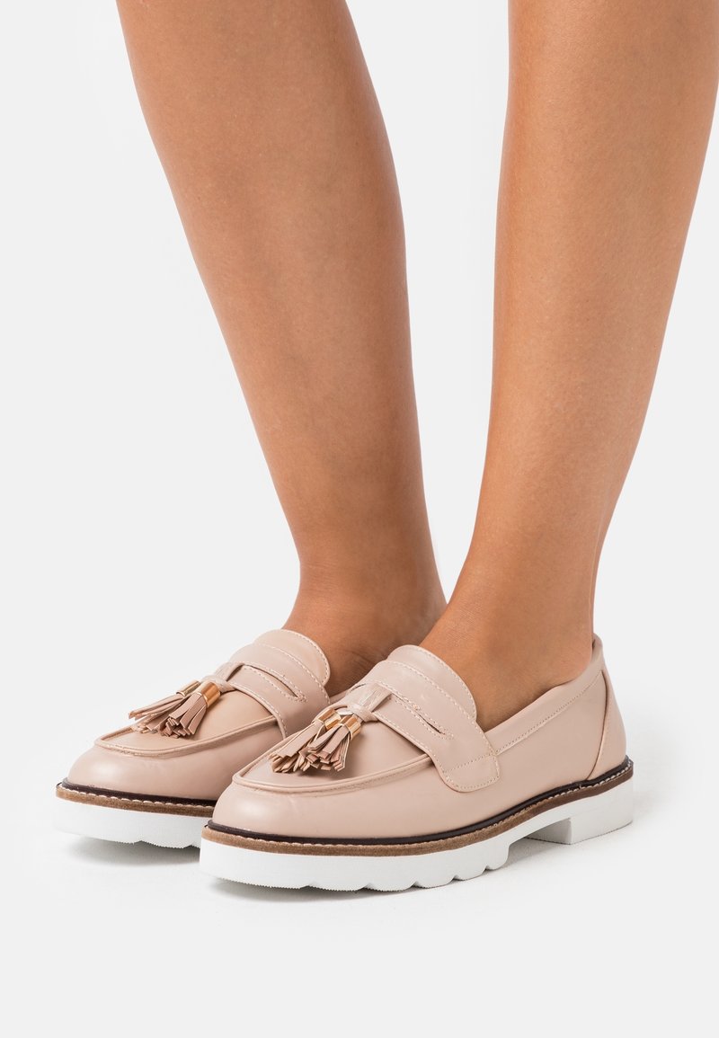 Mocassins en cuir rose clair avec détail à pompons, dotés d'une semelle épaisse blanche et d'un bord marron contrastant, vus de dessus.
