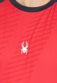 Rode sportshirt met een zwarte kraag, voorzien van een wit spinnenlogo en een subtiel diagonaal streepjespatroon over de stof.