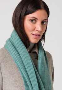 Una sciarpa in maglia a coste turchese si adagia su un maglione grigio, mettendo in risalto il suo tessuto testurizzato e il colore vibrante.
