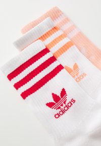 Trys porų įgulos kojinių: baltos su raudonomis juostelėmis ir logotipu, oranžinės su šviesesnėmis juostelėmis ir persikų spalvos. Minkšta, megzta medžiaga su raukšlėtais kraštais.
