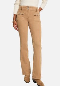 Pantalones de pana beige con pierna recta, dos bolsillos delanteros y cierre de tres botones. Textura suave con un sutil brillo, ideales para un look casual.