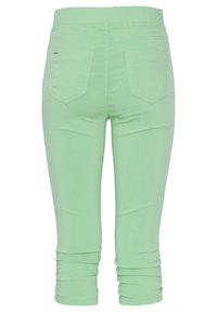 Leggings cortos de color verde claro hechos de tela elástica. Presentan una silueta ajustada con detalles fruncidos en los tobillos y dos bolsillos traseros.
