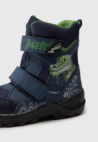 Botte pour enfants de couleur marine avec des accents verts et des sangles Velcro. Présente un graphisme de reptile, un mesh texturé et une semelle en caoutchouc avec un motif de traction.