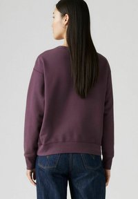 Burgundowa bluza z okrągłym dekoltem, ściągaczami przy rękawach i u dołu, o luźnym kroju i miękkiej teksturze, w połączeniu z ciemnoniebieskimi dżinsami.