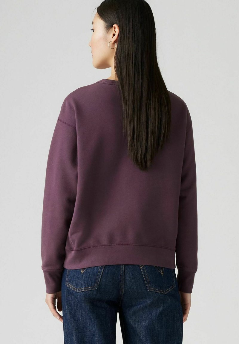 Bordeauxfarbener Sweatshirt mit Rundkragen, gerippten Bündchen und Saum, entspannter Passform und weichem Material, kombiniert mit dunkelblauen Jeans.